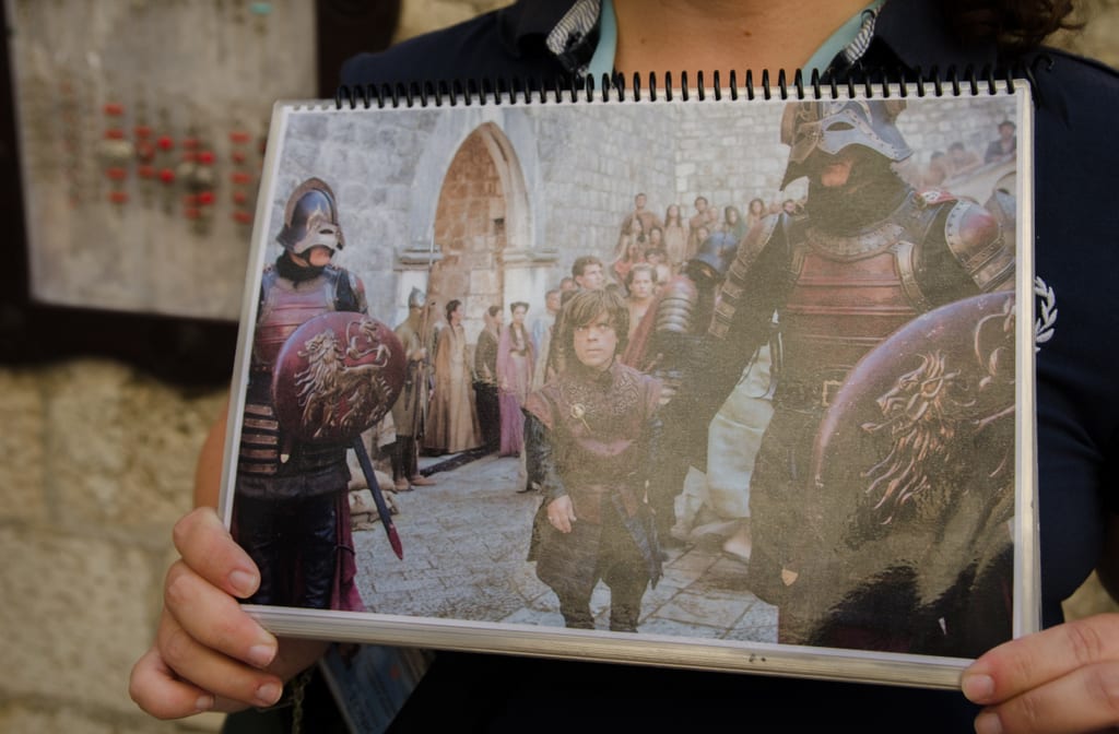 A set of hands in Dubrovnik holds a picture of a scene from Game of Thrones taking place in the Dubrovnik walls.