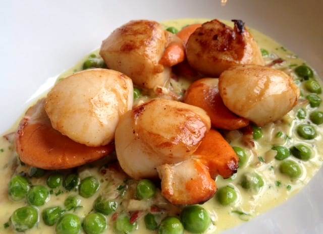 Five plump scallops sitting on a cream sauce with peas.