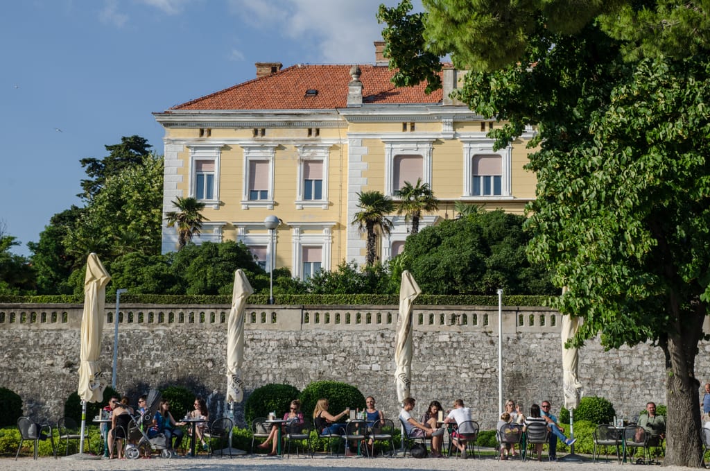 Street cafe scene in front of a yellow building in Zadar, Croatia.