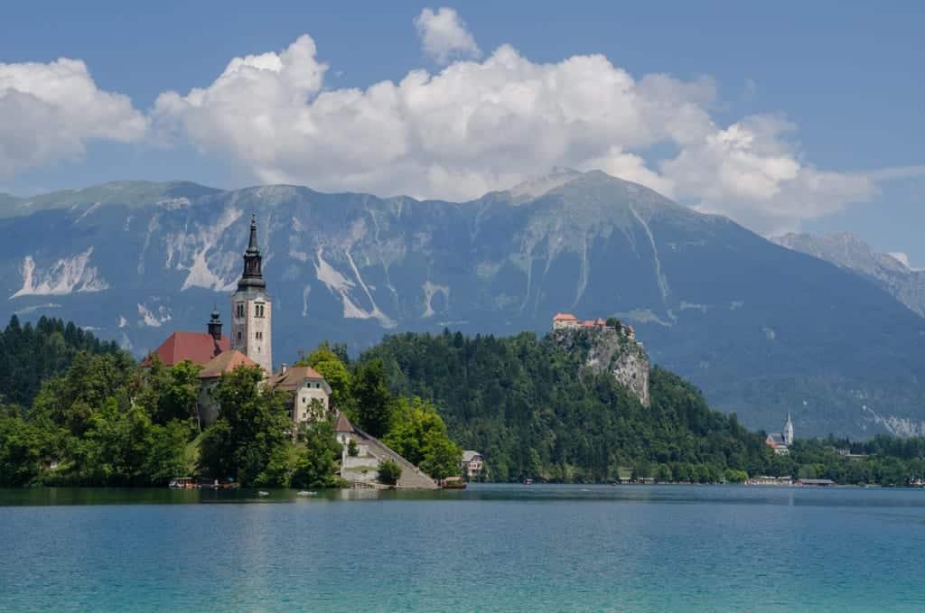 A tiny church on an island in a lake surrounded by mountains.