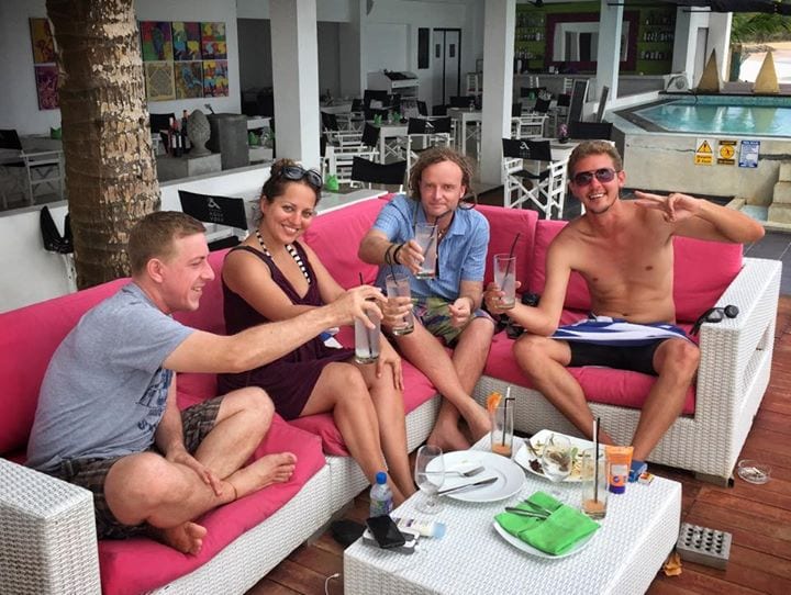 Kate and three male friends, sitting on a pink outdoor sofa and toasting drinks.