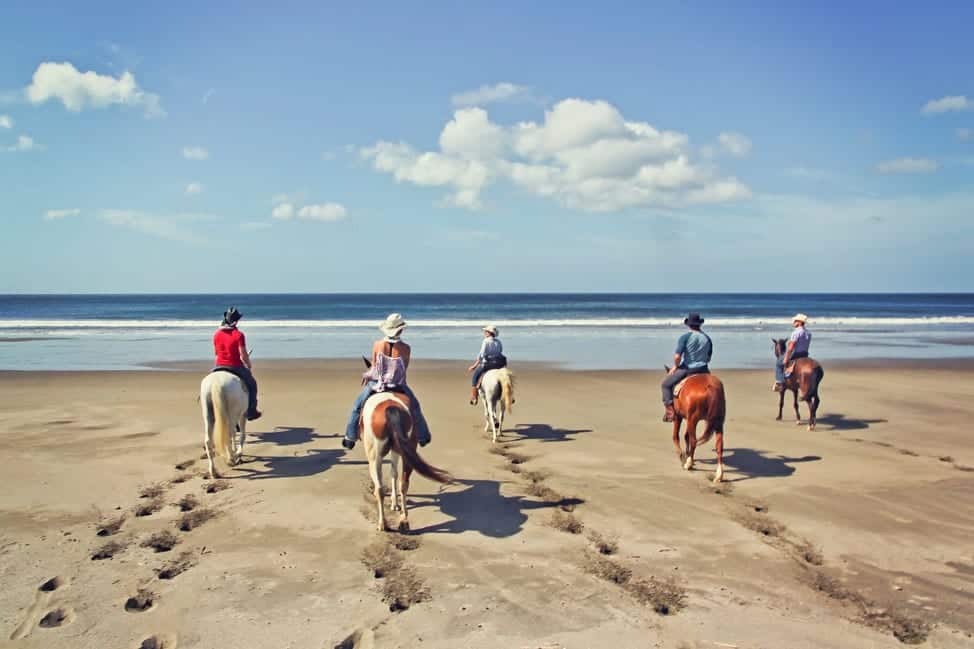 Five women on horseback on a beach, facing the sea.