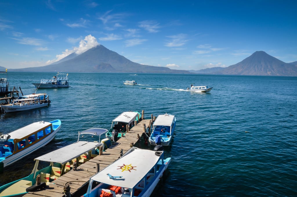 A bright blue lake covered with small white speedboats, two pointy volcanoes rising in the background.