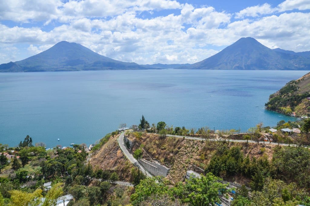 Curvy road on a cliff in front of Lake Atitlan, volcanoes in the background.