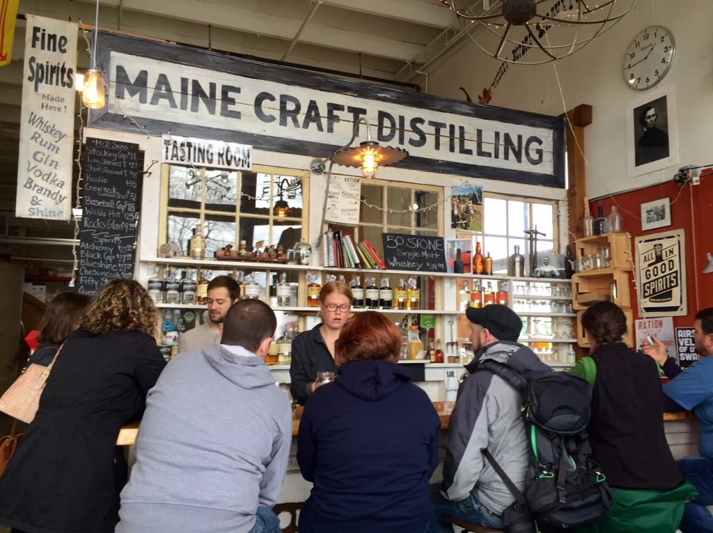 Customers sitting at a tasting counter with "Maine Craft Distilling" written on a sign.