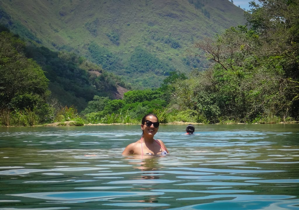 Kate smiling in sunglasses in the water, mountains rising behind her.