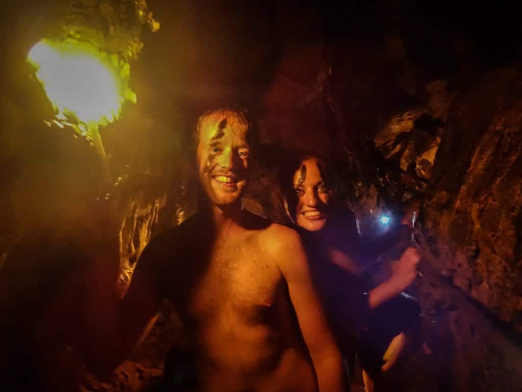 Kate and Shaun in a cave, with war paint on their faces, holding a torch and grinning.