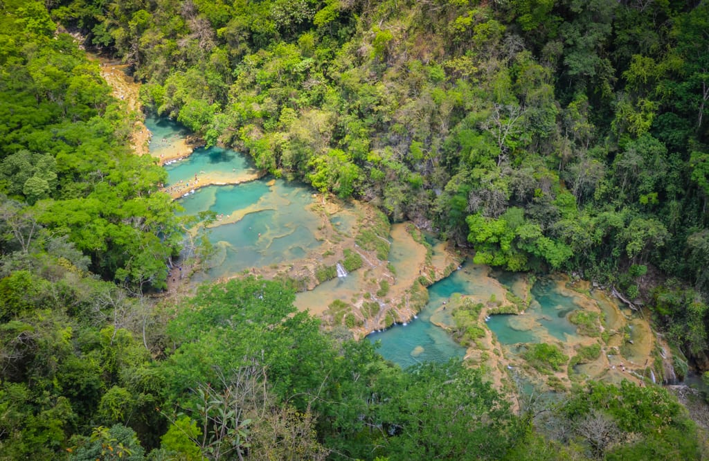 Aerial view of the multi-tiered turquoise lakes, waterfalls in between, surrounded by forest.