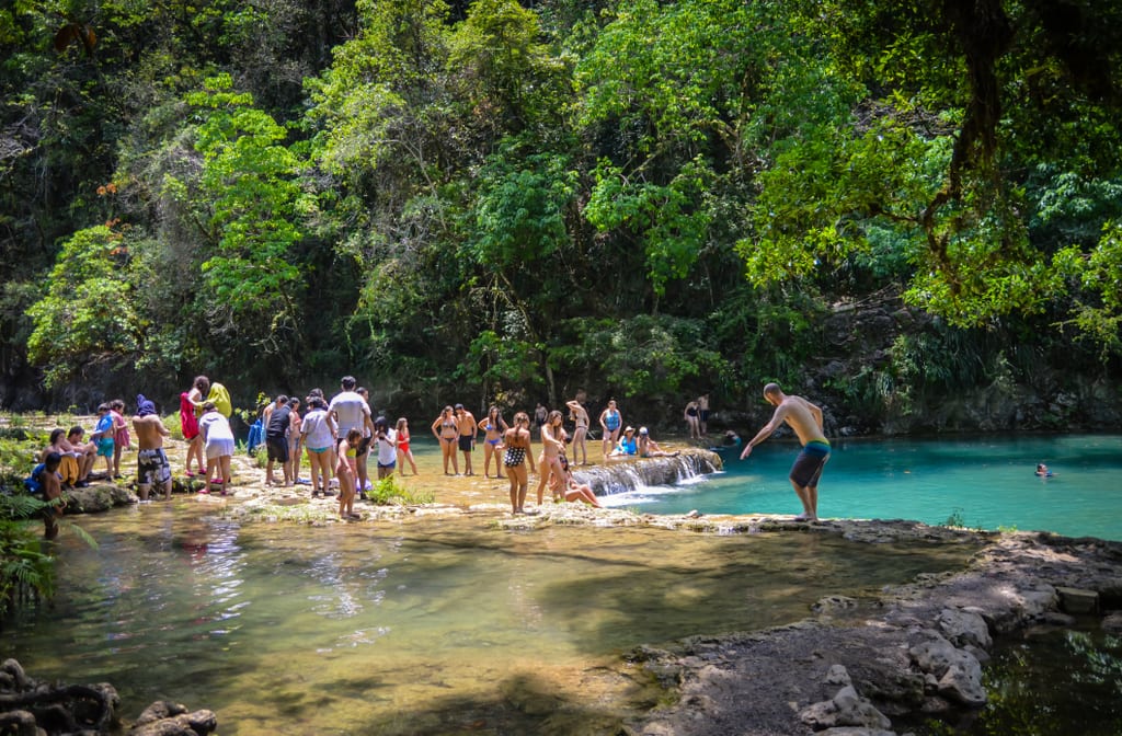 People on the edge of one of the pools at Semuc Champey, one boy standing as if he's afraid to jump in.