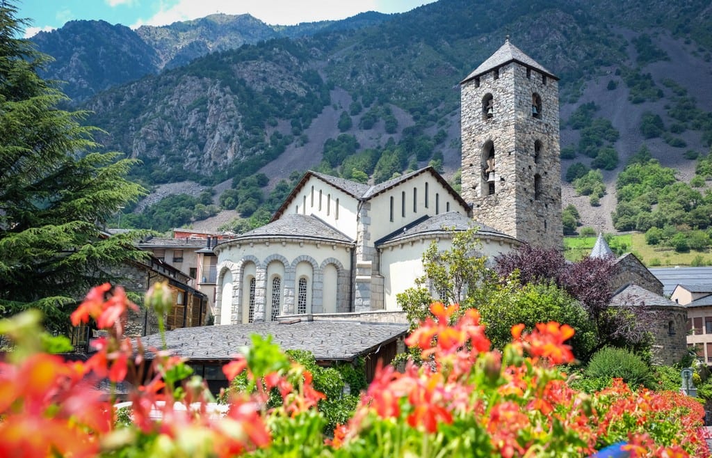 A church among the mountains of Andorra, bright red flowers in front.