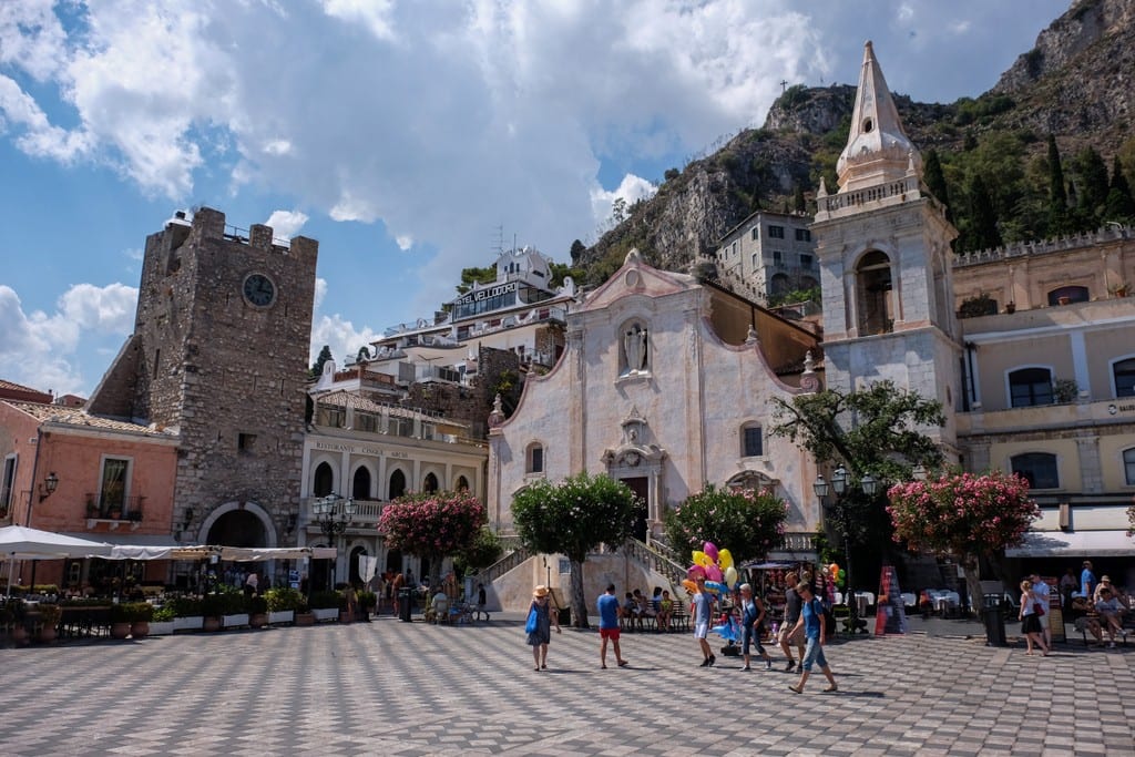A piazza in Taormina with a church and black and white chess board-like tiles on the square.