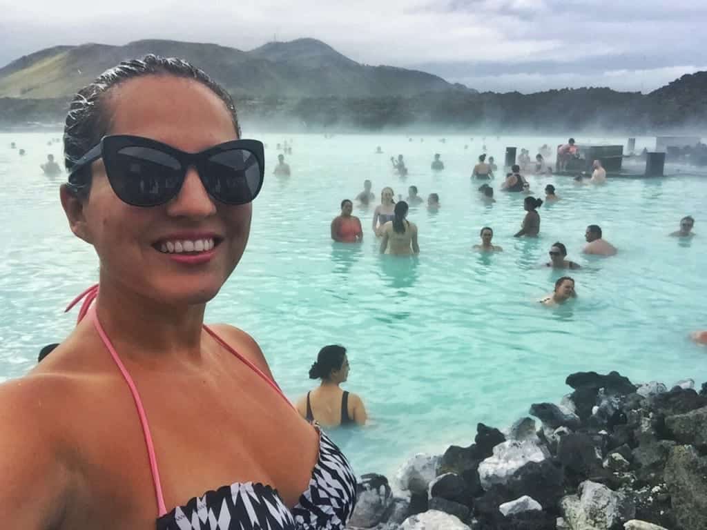 Kate takes a selfie in the Blue Lagoon in Iceland, steaming bright blue water behind her with people in the water.
