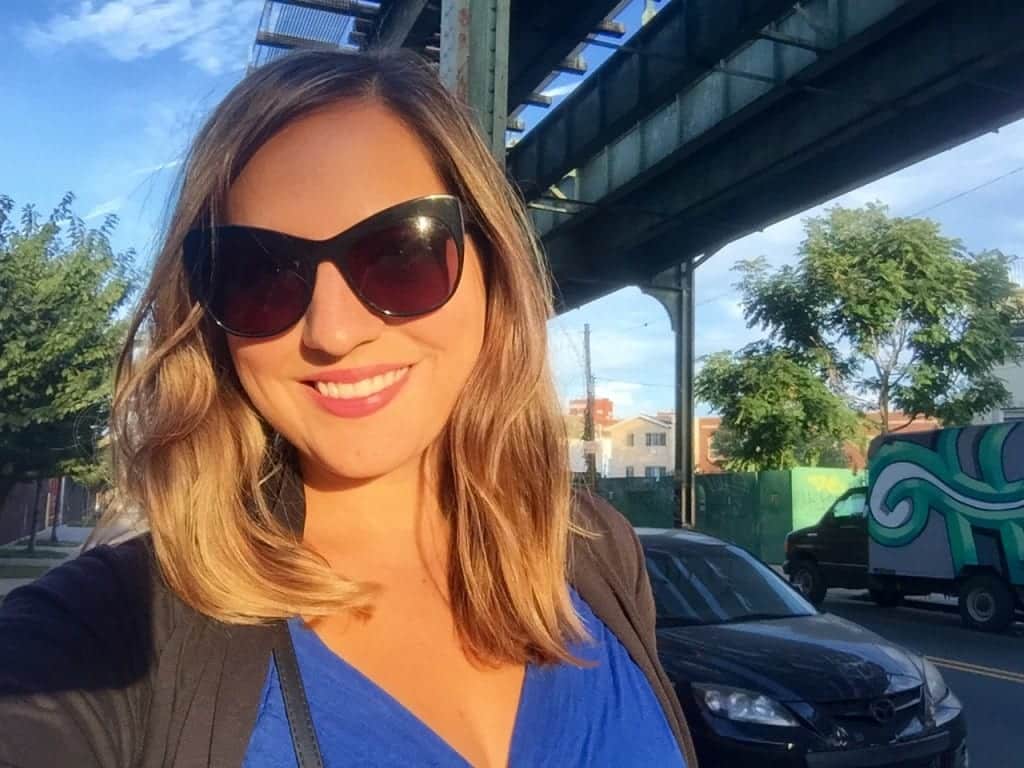 Kate with blonde hair and sunglasses, standing beneath a subway platform in Bushwick, Brooklyn.