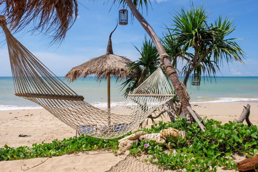 A hammock and straw umbrella palapa on Relax Bay, Koh Lanta, Thailand, clear turquoise water and the beach.