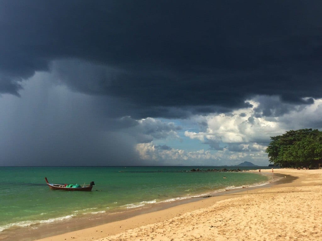 An extremely dark storm cloud over the sunny beach and blue-green water of Koh Lanta.