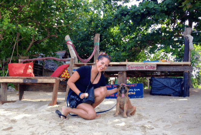 Kate pets a brown puppy named Monroe on a beach in Thailand.