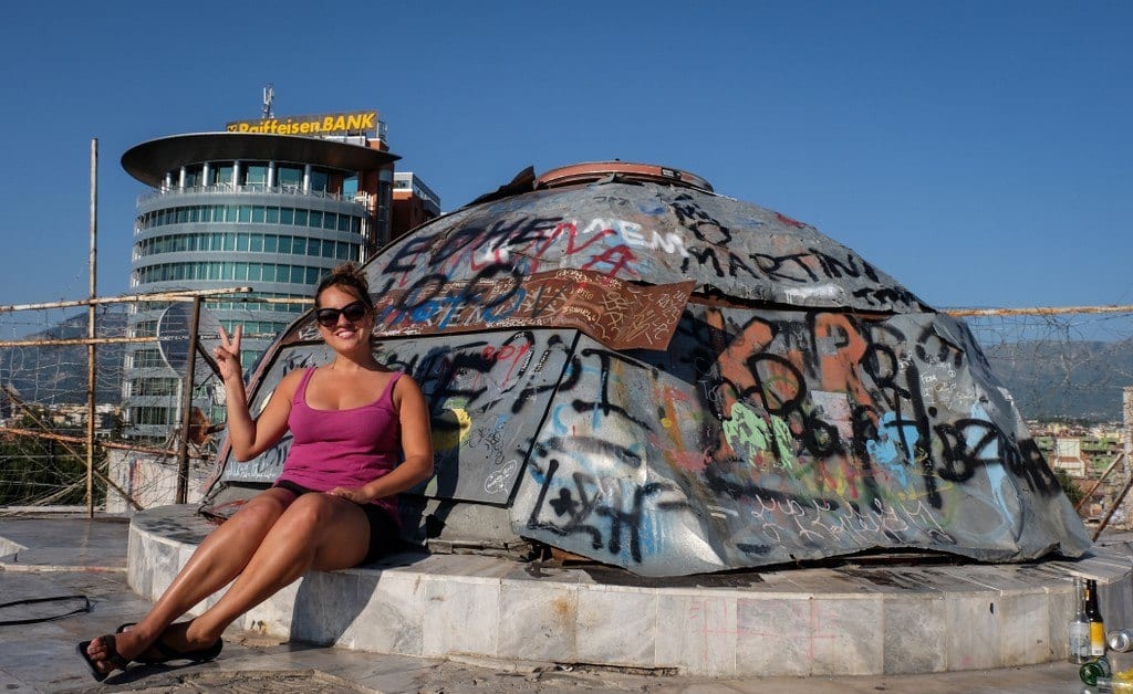 Kate gives a peace sign while sitting in front of a graffiti-covered dome on top of the pyramid in Tirana.