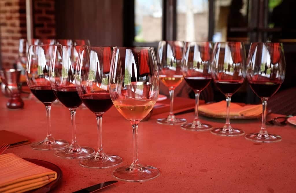 Two sets of four glasses of wine arranged across from each other at Bottega restaurant in Yountville, California. Each setting has three glasses of red and one glass of white and they are filled generously.