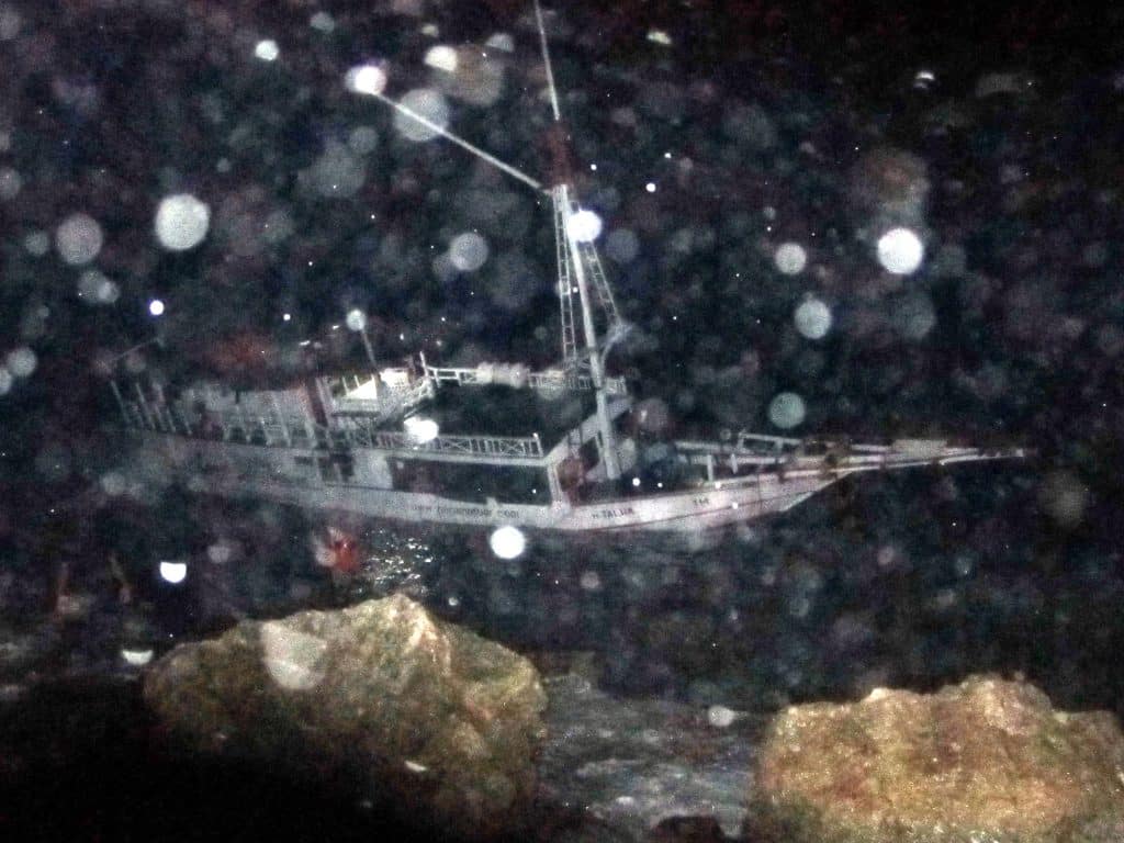 A shipwrecked wooden boat leaning to its side in a rain storm