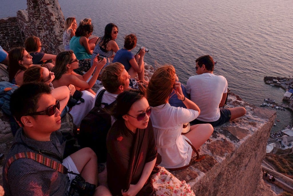 People lit with red light, sitting on a ledge in Santorini, waiting for sunset.