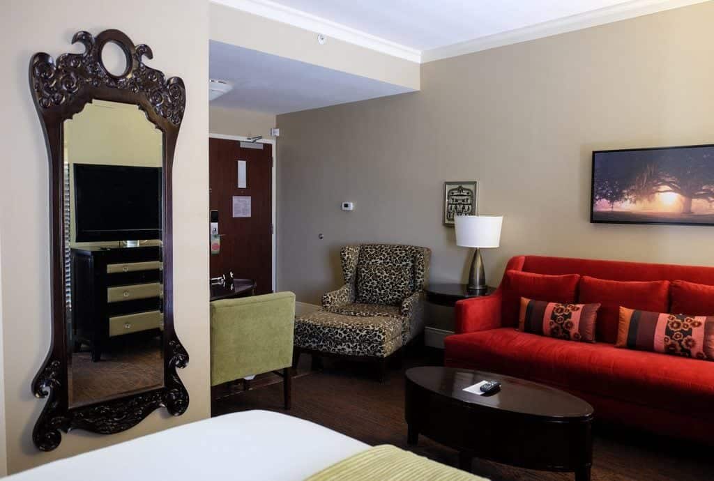 The hotel room at the Andaz Savannah. An ornate wooden mirror, bright red couch with pillows, and funky leopard-print chair and matching footstool.