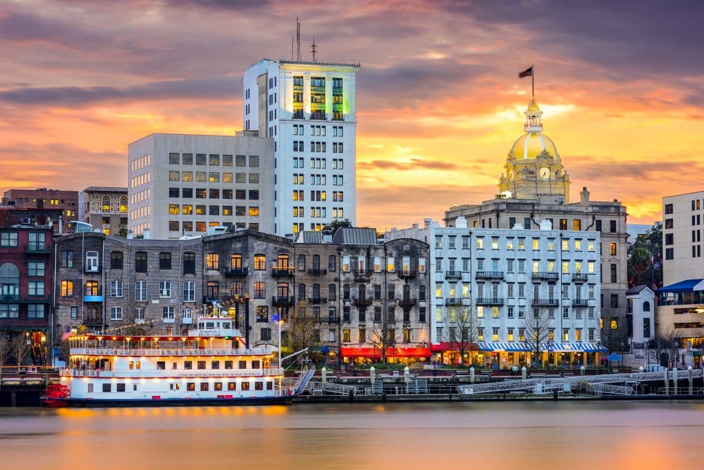 Riverboats parked on the banks of the Savannah River at sunset, a sunset and high-rise buildings in the background.