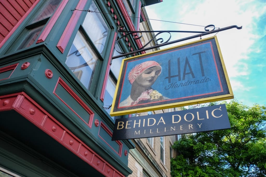 A sign reading "Hat Handmade - Behida Dolic Millinery" hanging from a window.