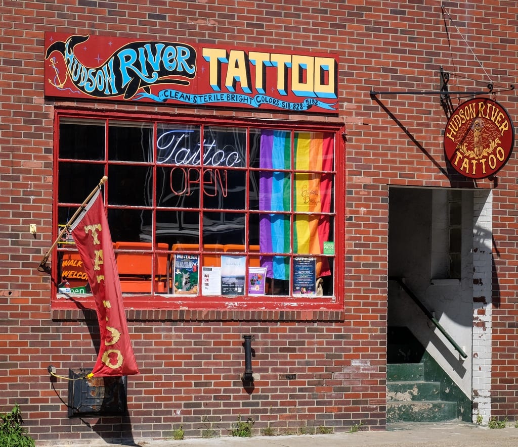 A brick building with a pride flag and a sign reading Hudson River Tattoo.