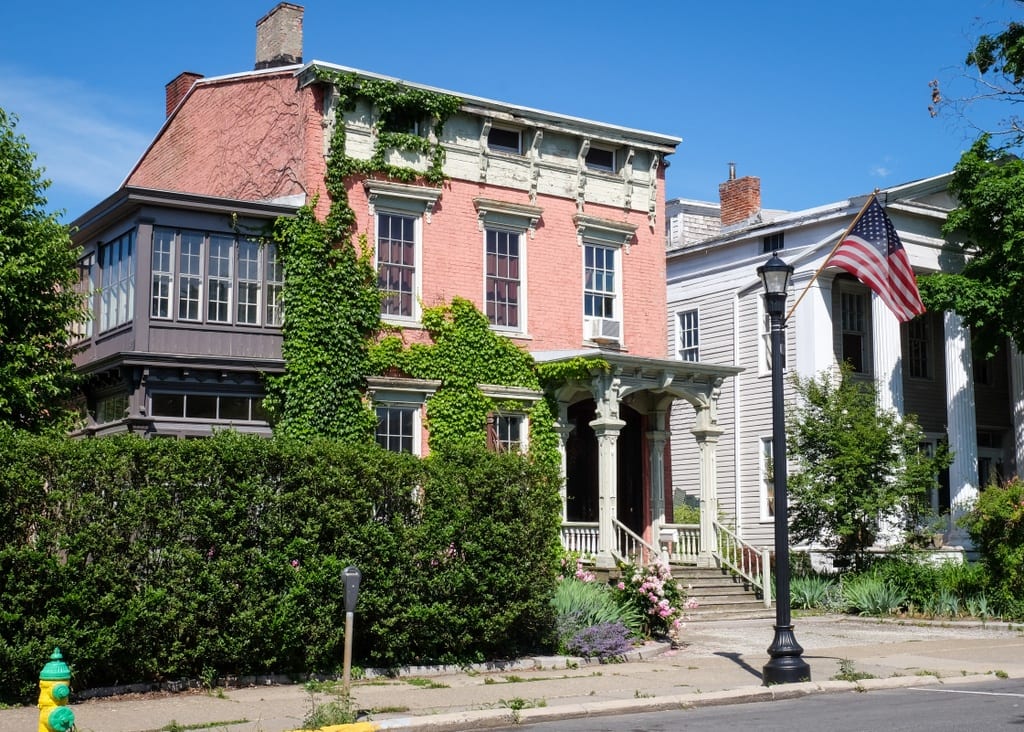 An old-fashioned brick building covered in Ivy with an ornate wooden porch with columns.