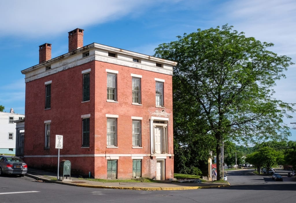 A small detached brick building next to a tall green tree.