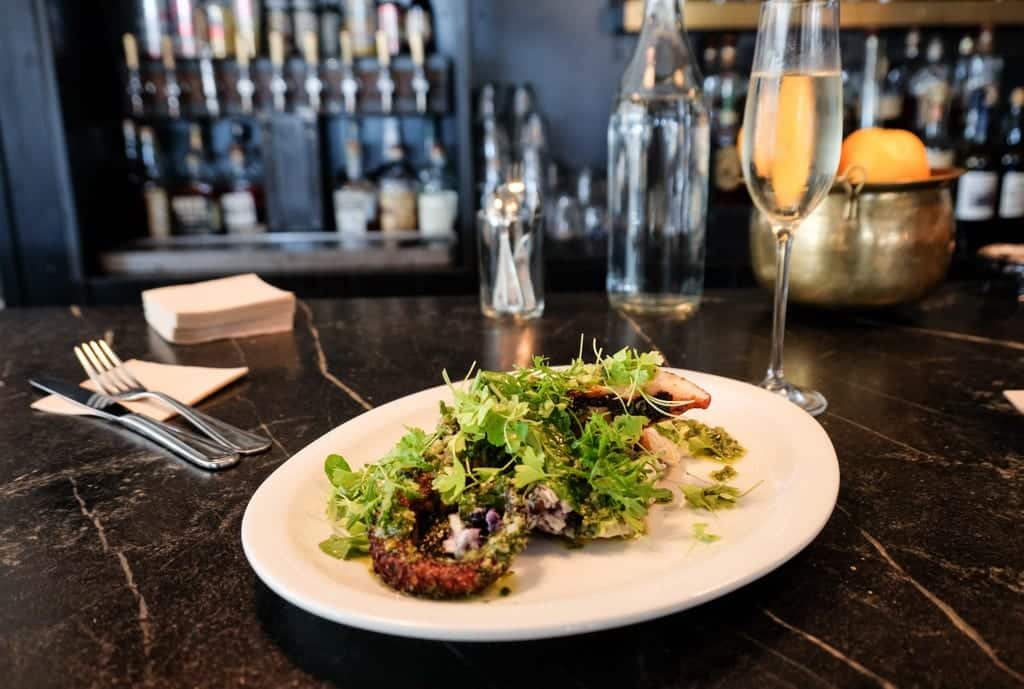 Grilled octopus underneath a variety of greens next to a glass of champagne.