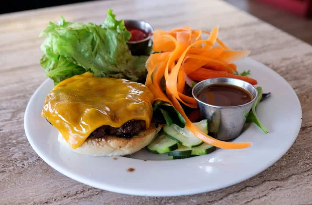 An open-faced cheeseburger with a yellow melty piece of cheese on top, served next to a salad with long carrot ribbons.