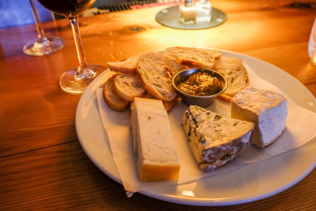 A cheese plate with three types of cheese, crostini, and jam.