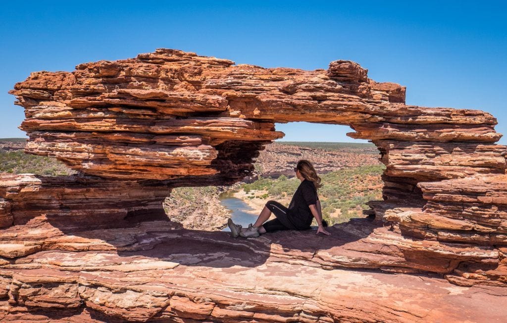 Kate sitting in the arch of a red rock formation in Kalbarri, Western Australia.