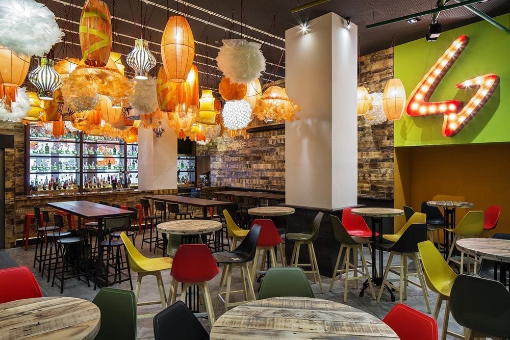 Small tables with brightly colored chairs inside the Generator Hostel Barcelona