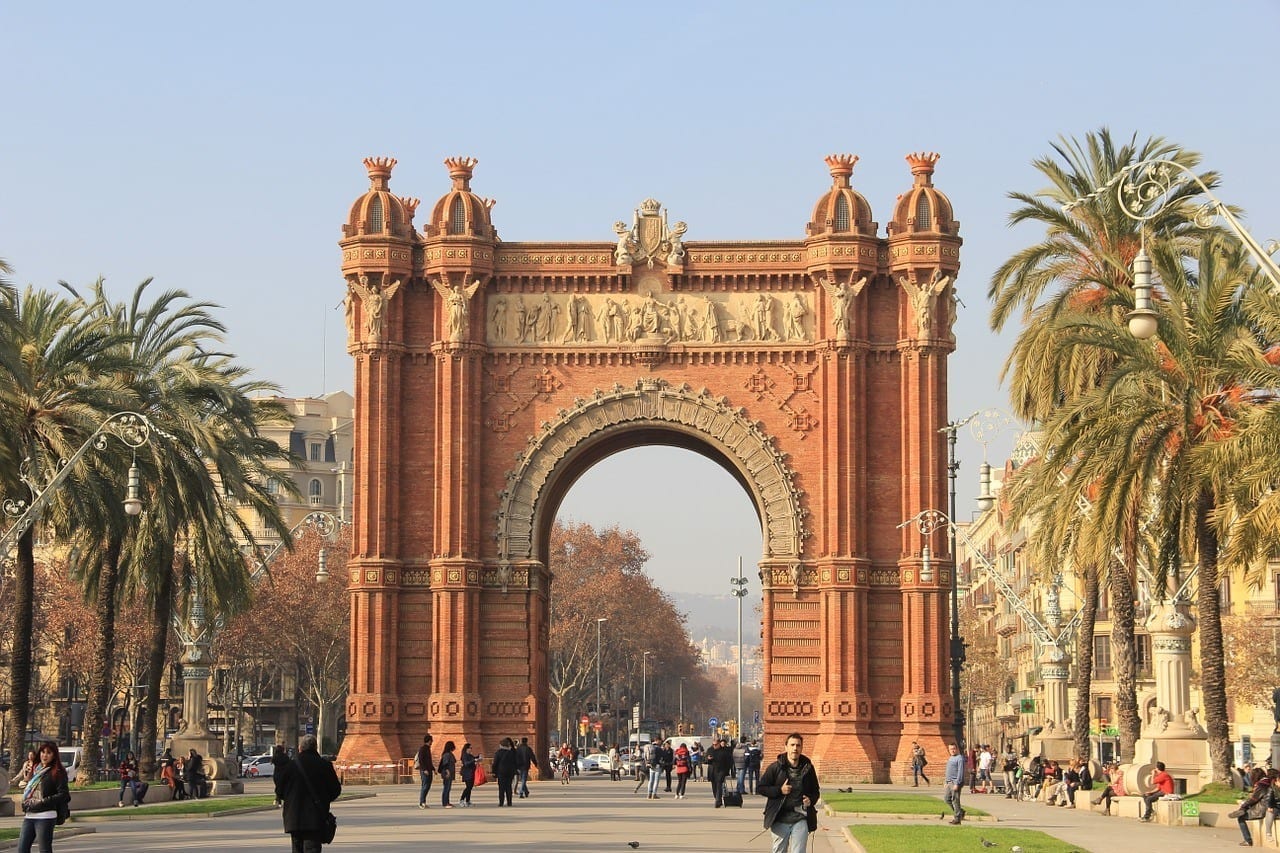 Barcelona's red-colored "Arc de Triomf, tall palm trees on each side of it.