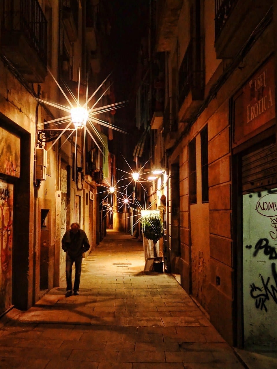 A dark side street in Barcelona; the street lights have points like stars. 