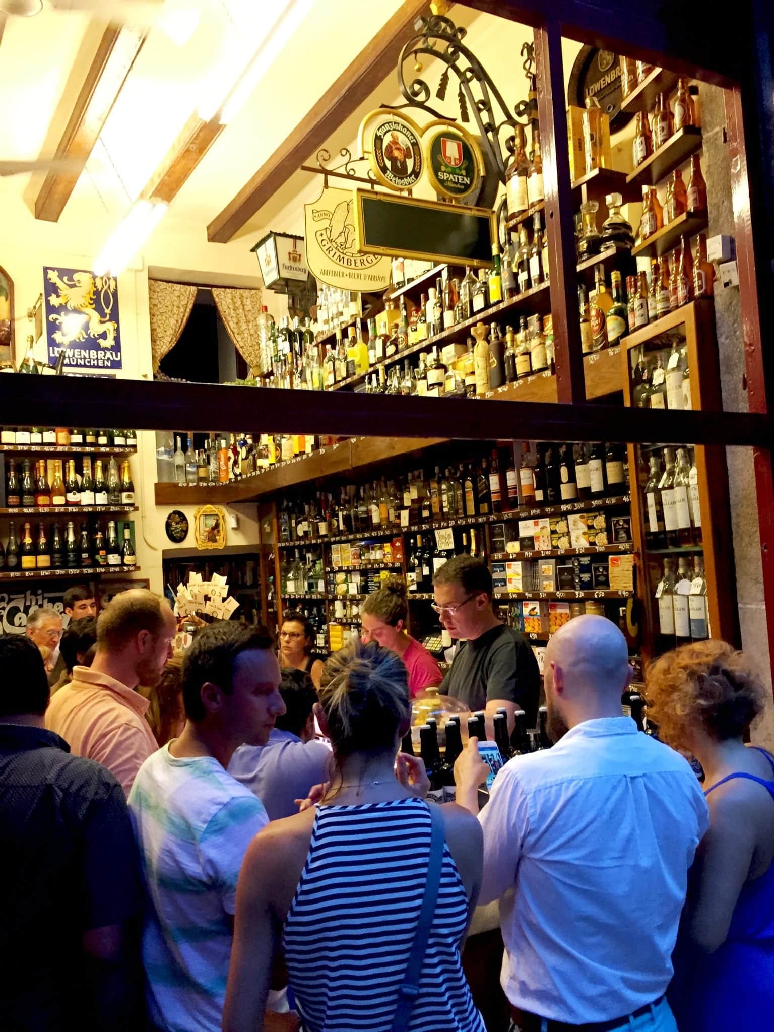 People gathered around a bar in Barcelona, with two walls lined with bottles of liquor