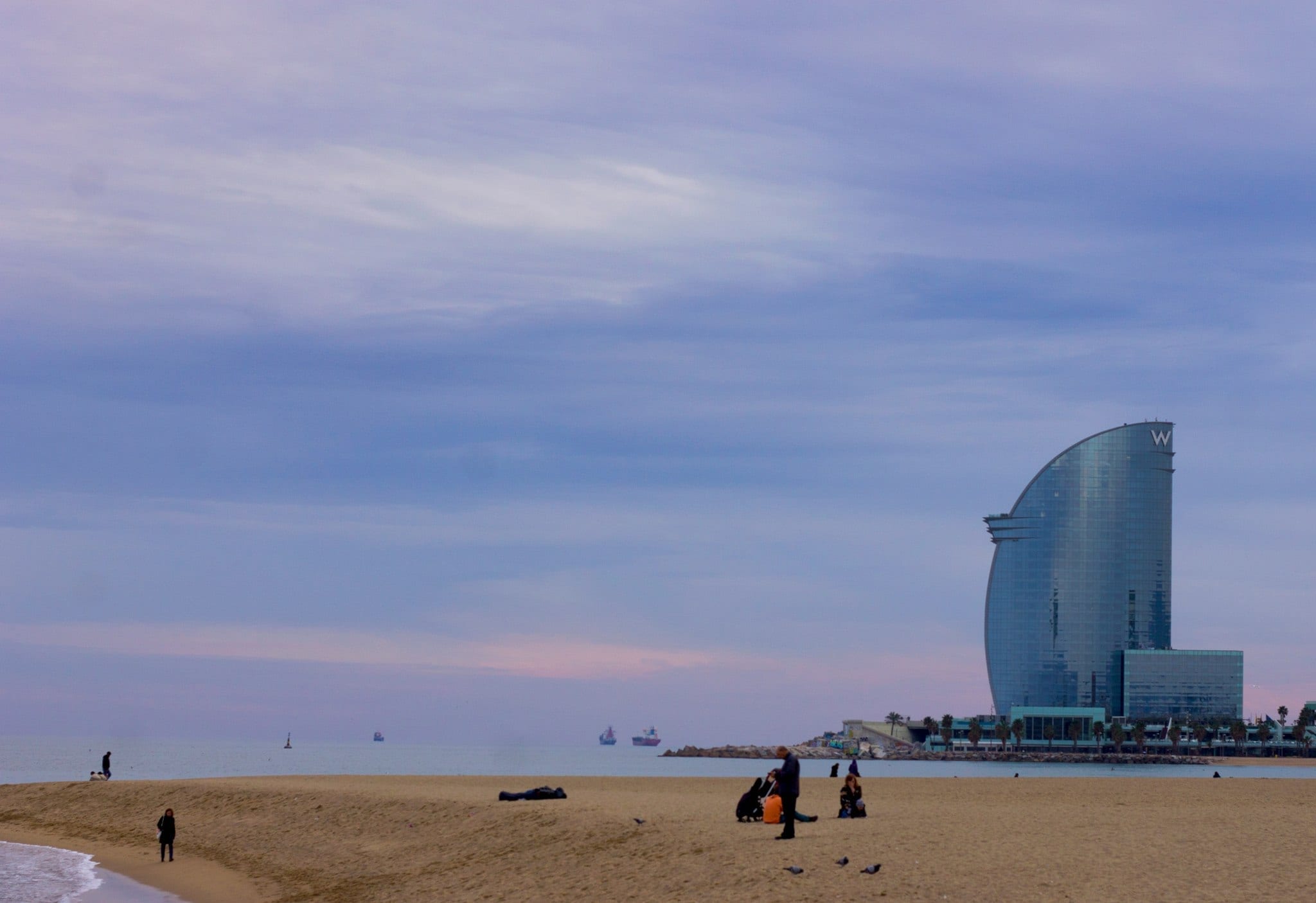 A few people on the beach with the W Barcelona in the background