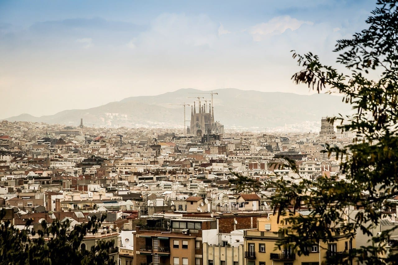 A faded view of Barcelona from above. You see the spires of the Sagrada Familia poking far above the rest of the buildings.