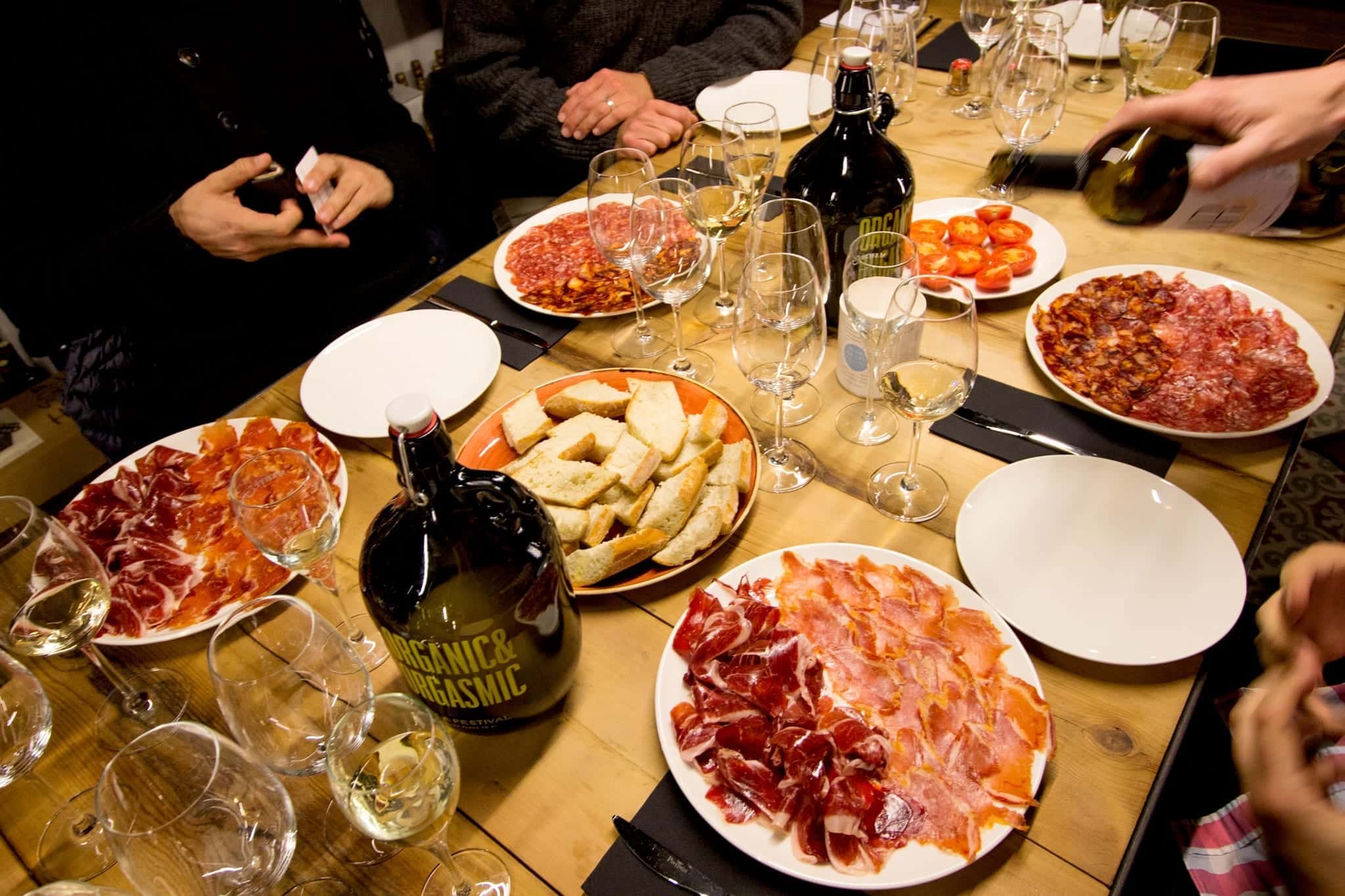 A table of tapas and wine glasses, with a hand pouring a bottle of wine