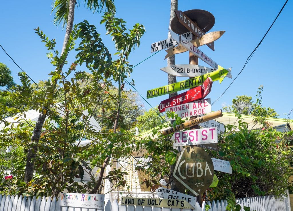 A pole topped with several wooden small signs pointing to different cities around the world.