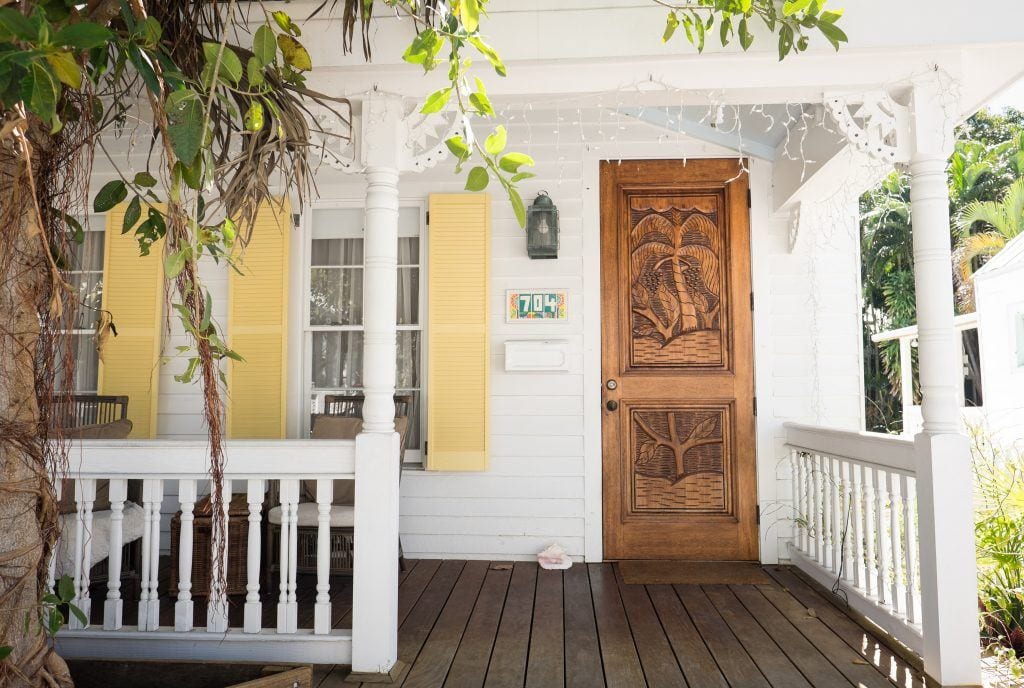 A white cottage with a porch and dark wooden front door in Key West