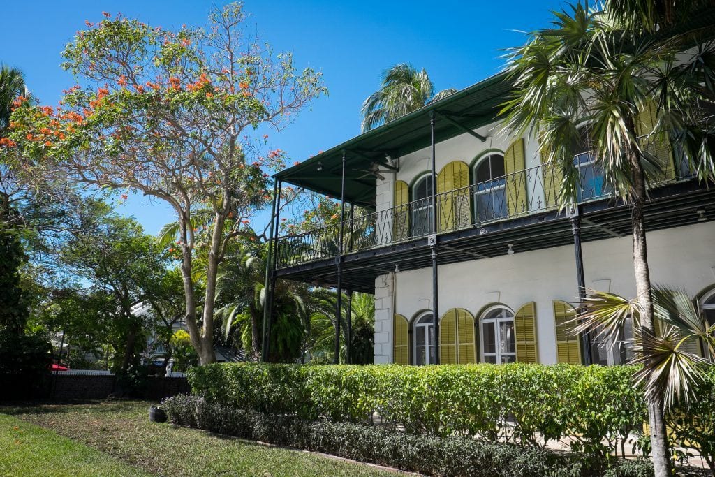 La maison d'Hemgingway, une grande maison blanche avec des volets jaunes et des porches enveloppants à Key West.