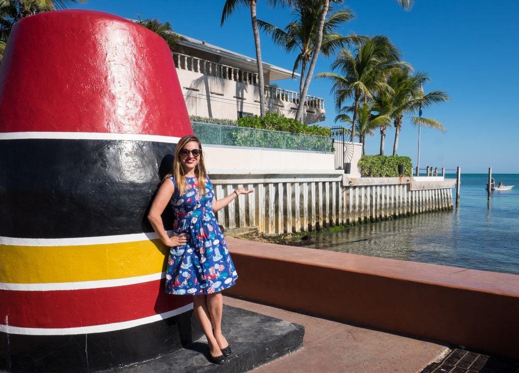 Kate standing in front of the southernmost point buoy in Key West, wearing a retro-style blue dress.