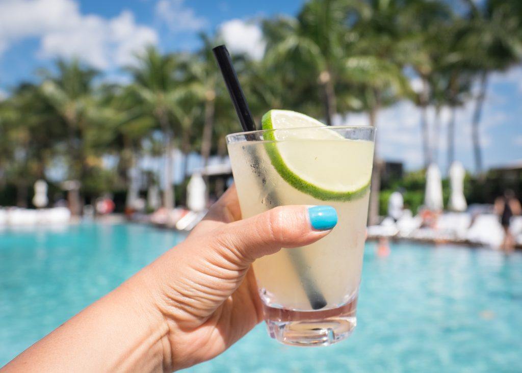 Kate's hand with a bright turquoise painted thumbnail holding a margarita in front of the bright turquoise pool at the W South Beach.