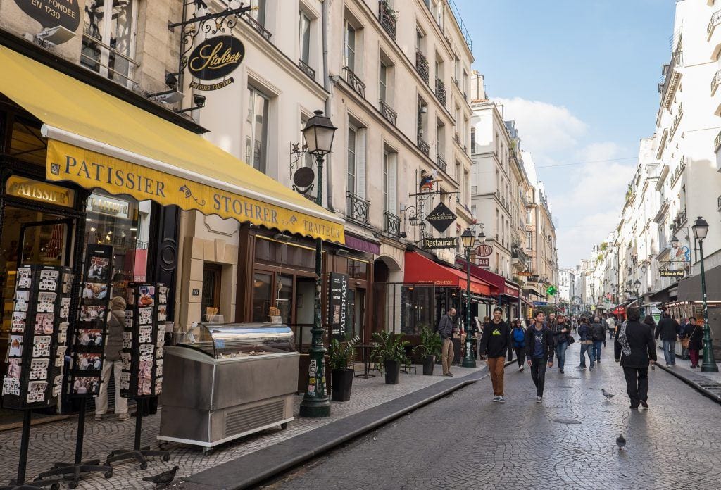 AN angled view of Rue Montorgueil in Paris with pedestrians walking down the street and a yellow awning to the right