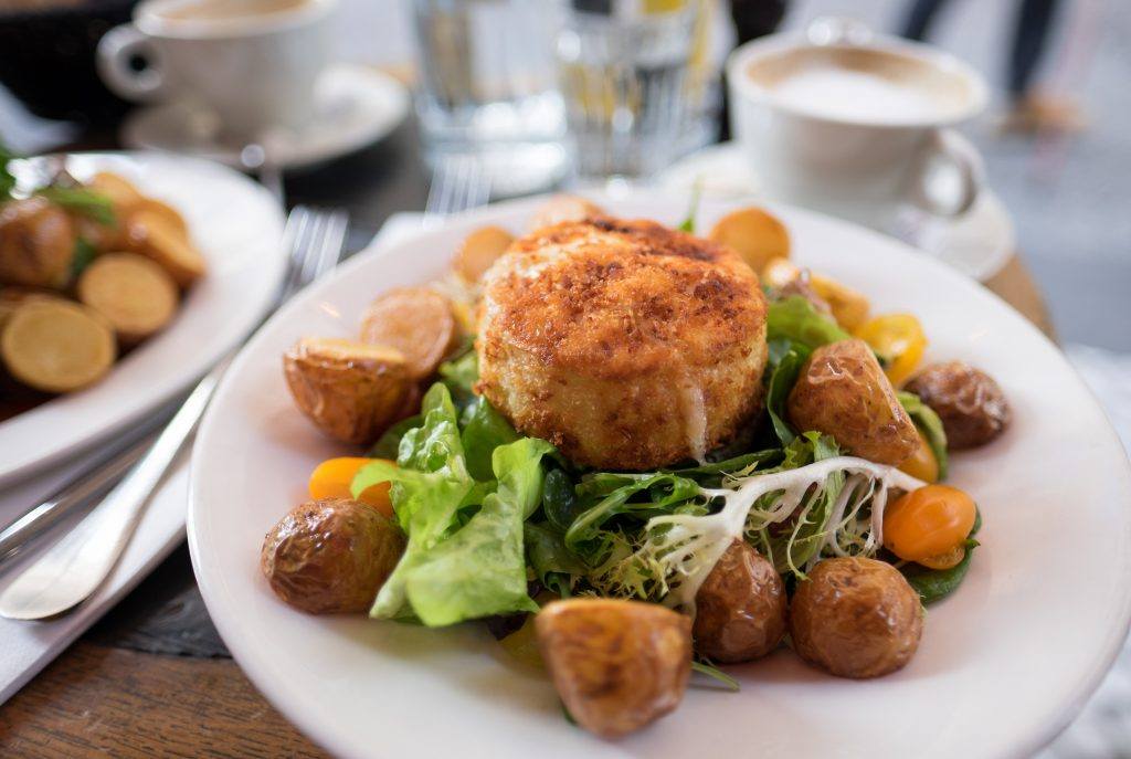 A plate of food with a breaded item on top of a salad and roasted potatoes
