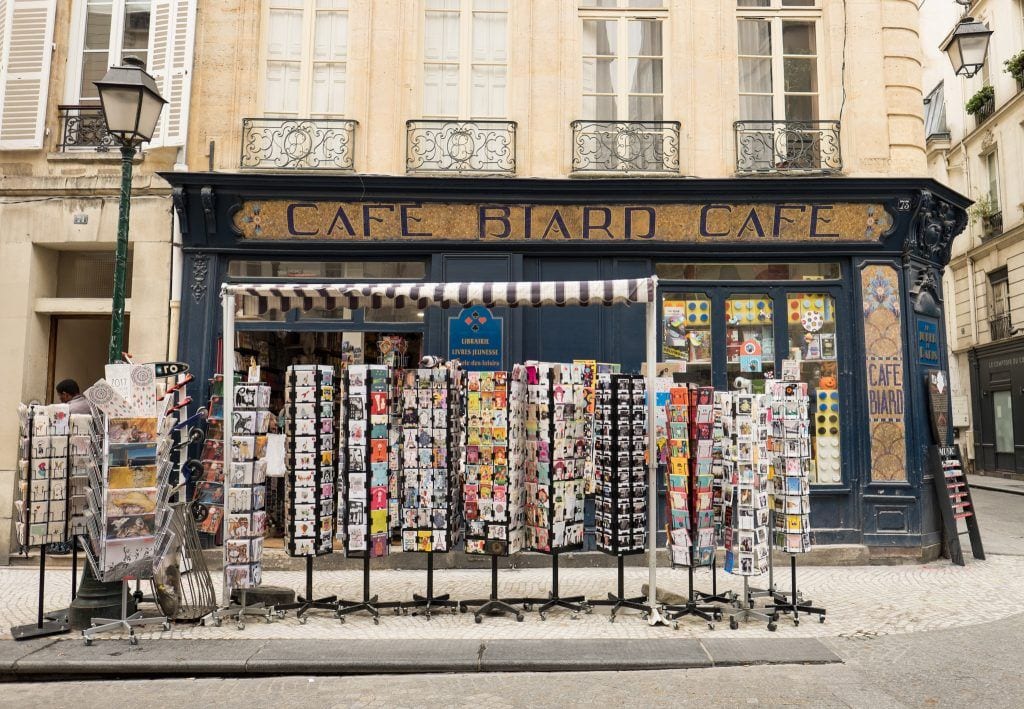 Exterior of a cafe in Paris with a selection of postcards and magnets set up for sale