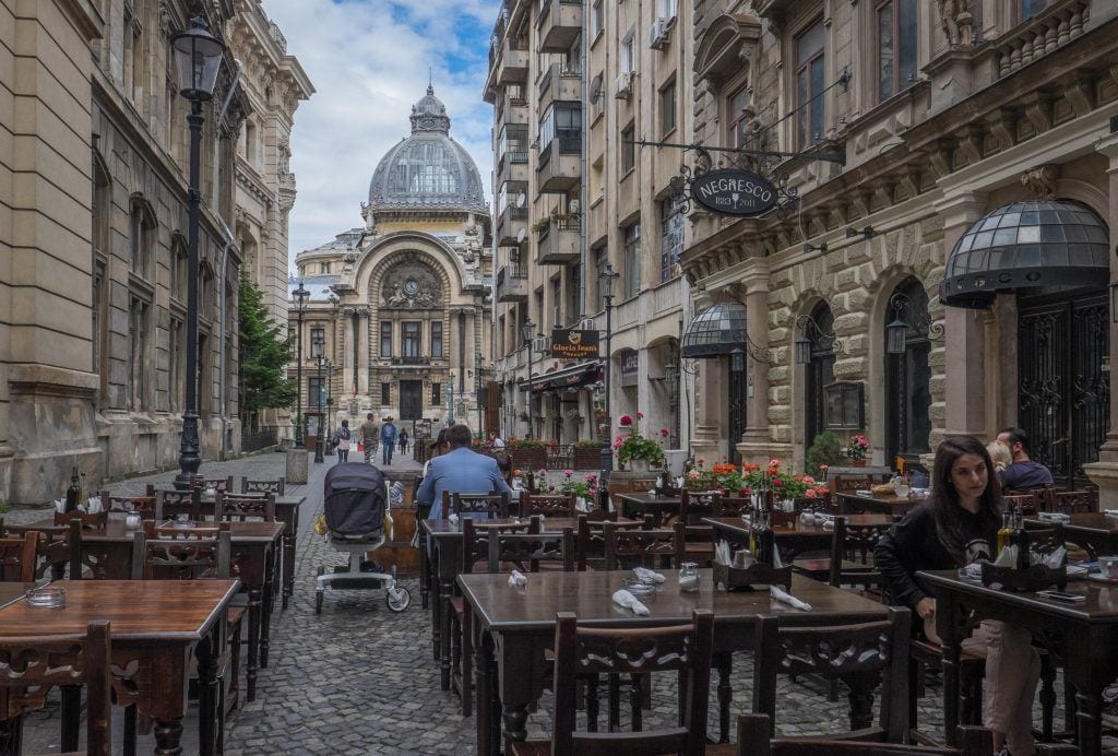 A domed church-like building in the distance in Bucharest, a street with sidewalk cafes in the foreground.